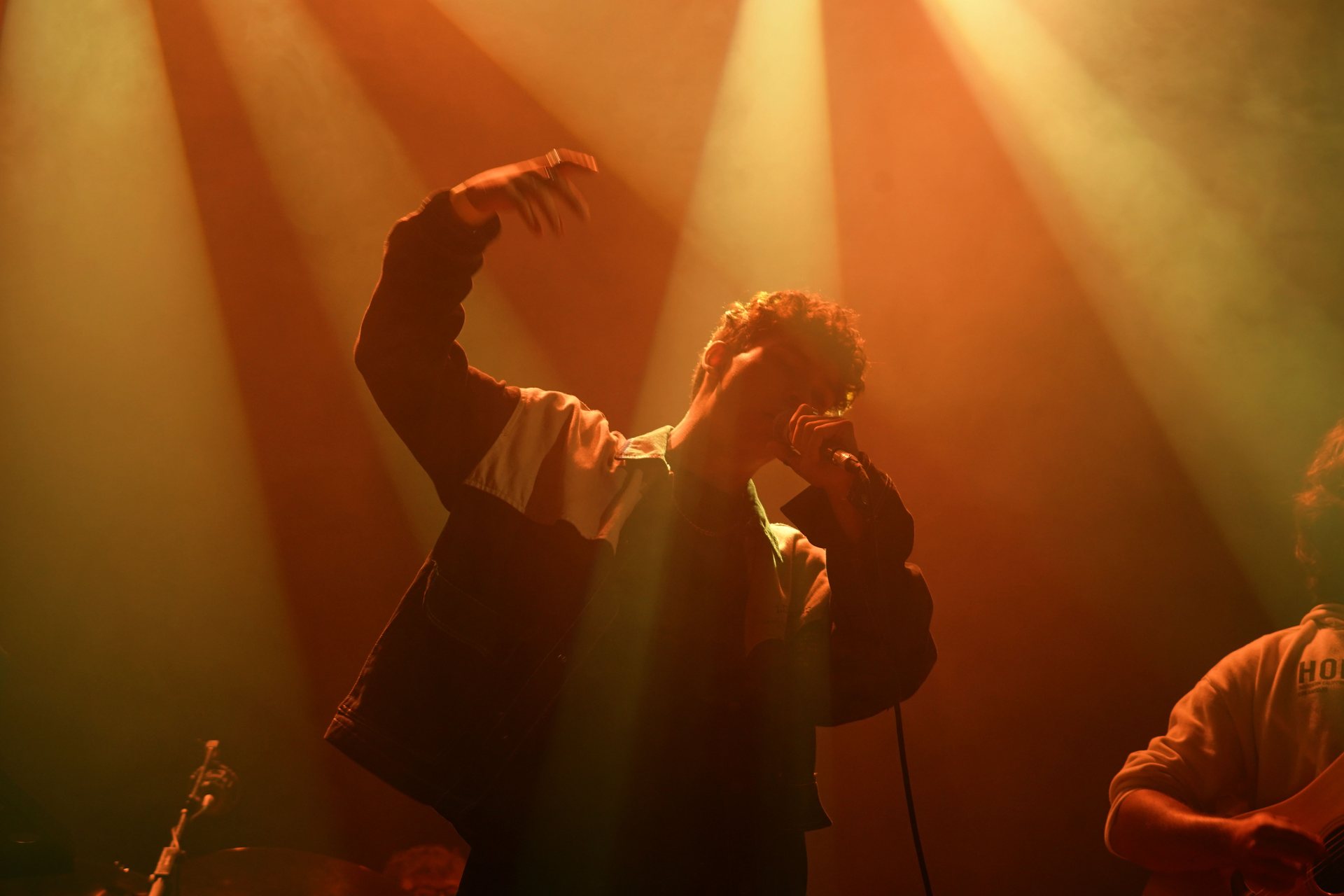 Stephen Mathes with both arms raised, lit from behind in amber haze