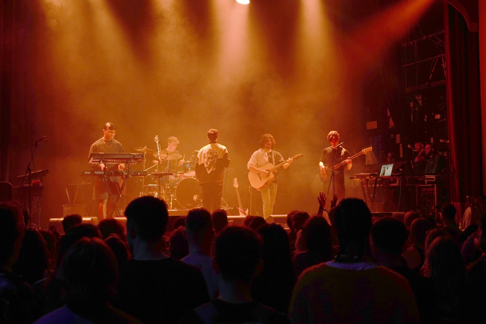 The full five-piece band mid-set in warm amber light above a crowd