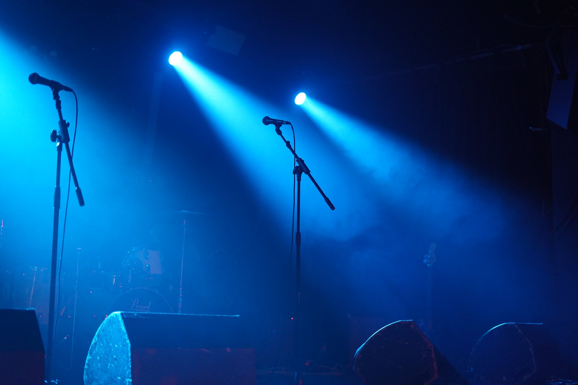 A microphone stand lit by crossing blue beams with the band behind it
