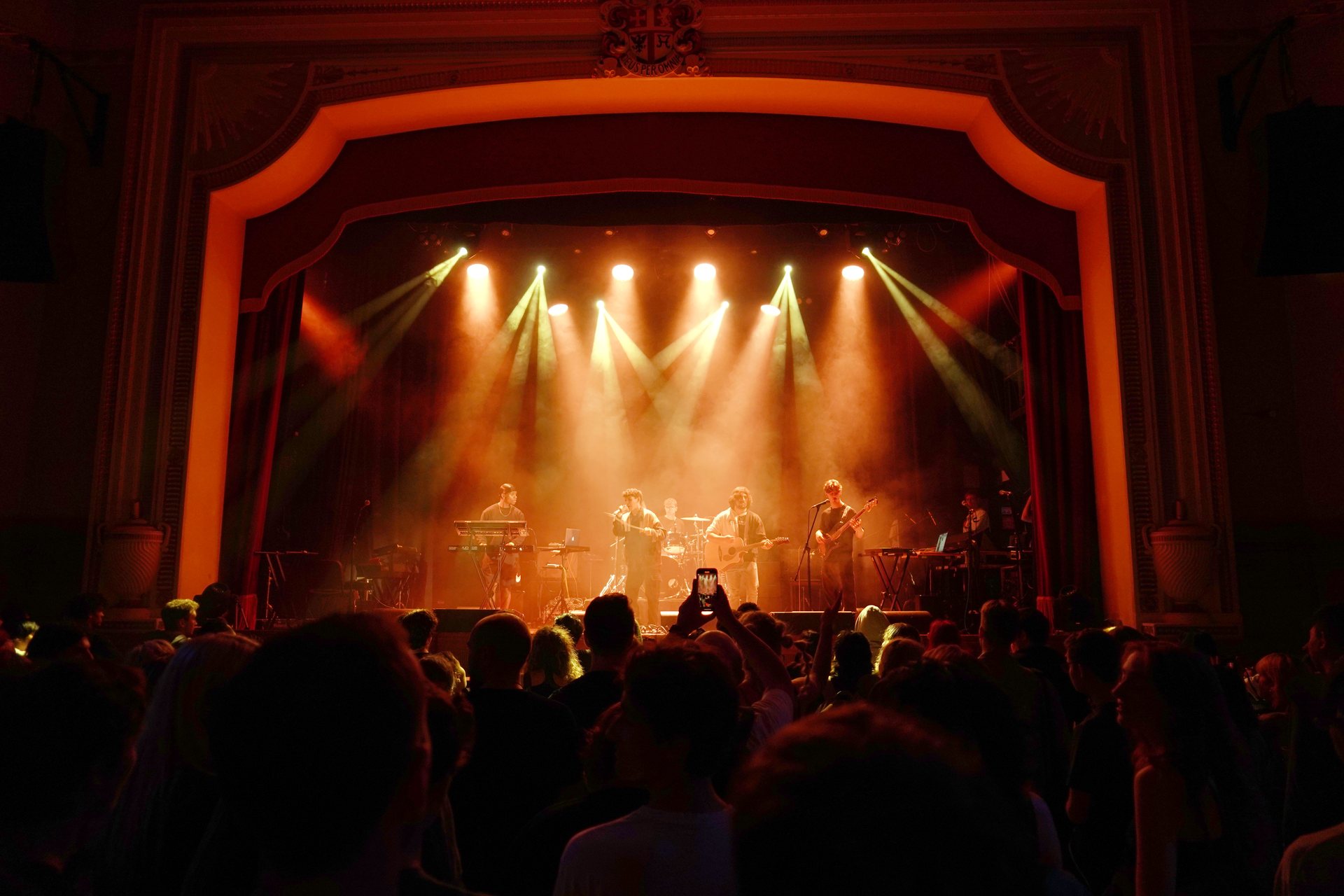 The Islington Assembly Hall proscenium arch lit in deep red above a packed floor