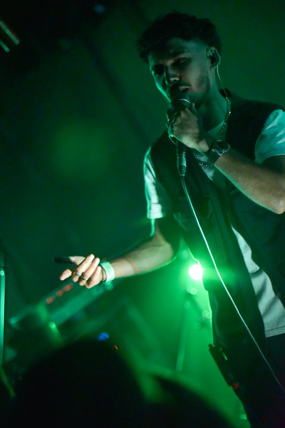 Stephen Mathes singing into a handheld microphone with his arm out to the crowd, lit green at Pioneer Club