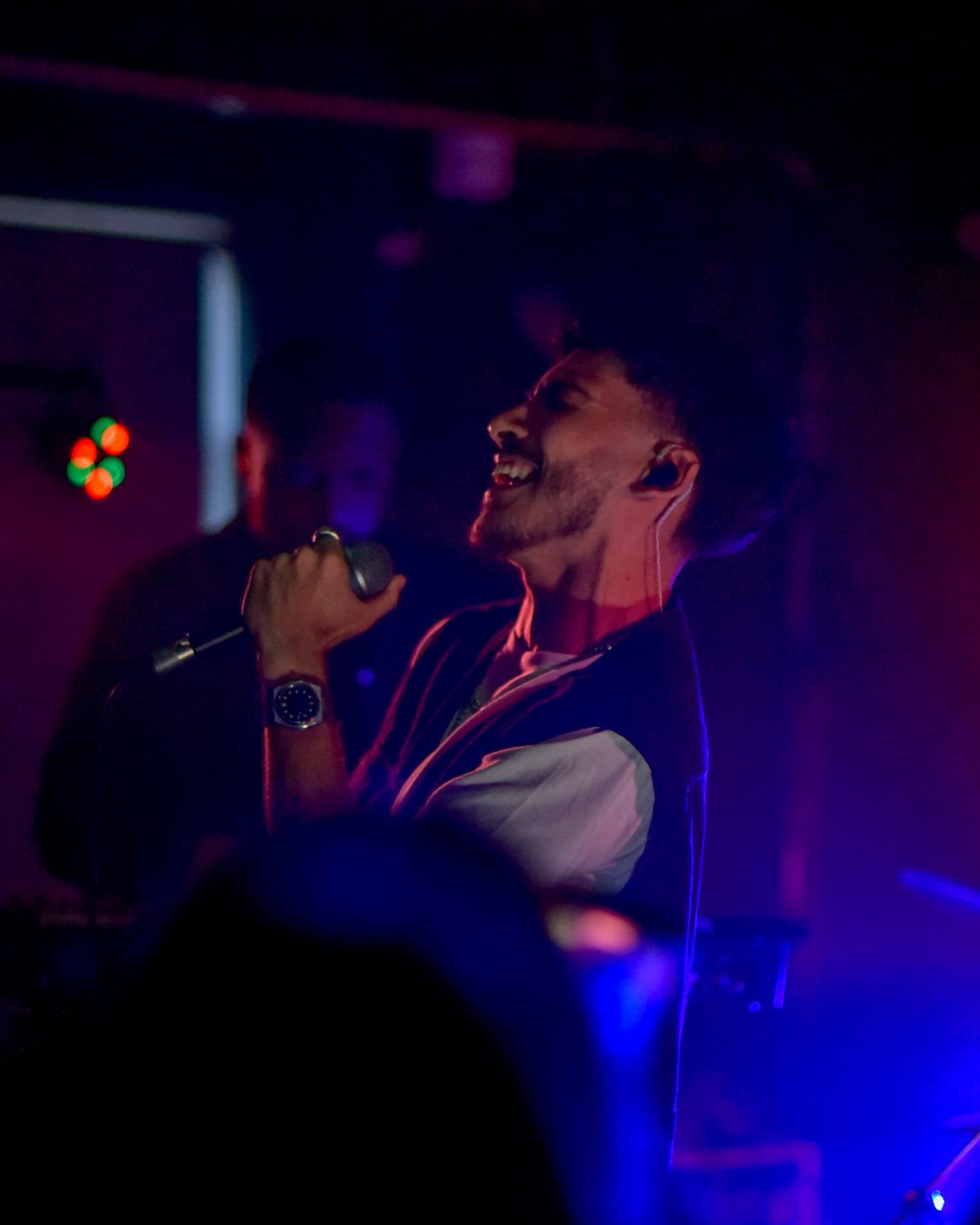 Stephen Mathes singing into a handheld microphone under red and blue stage light